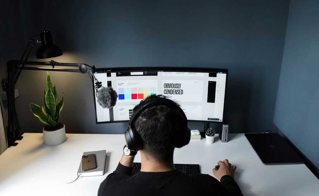 Top-down view of SEO professional working at a clean desk with a large monitor, headphones, and a plant beside the workspace.