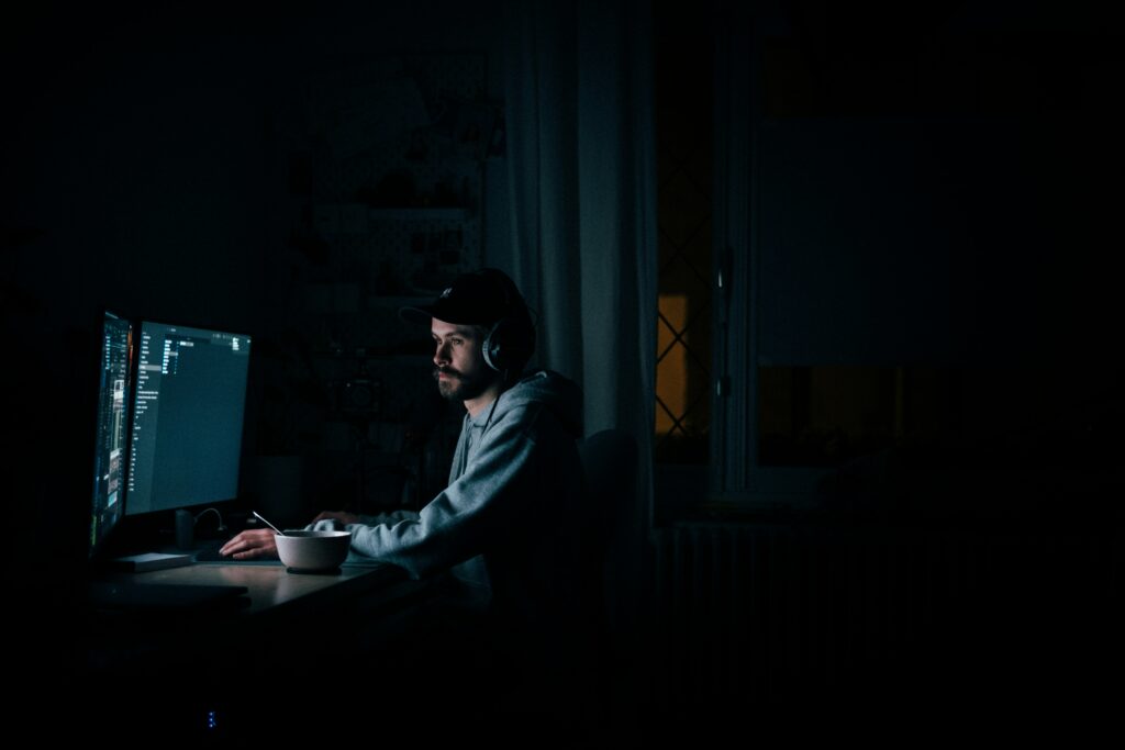Freelancer wearing headphones, working on dual monitors at night, focused on website optimization and digital marketing.
